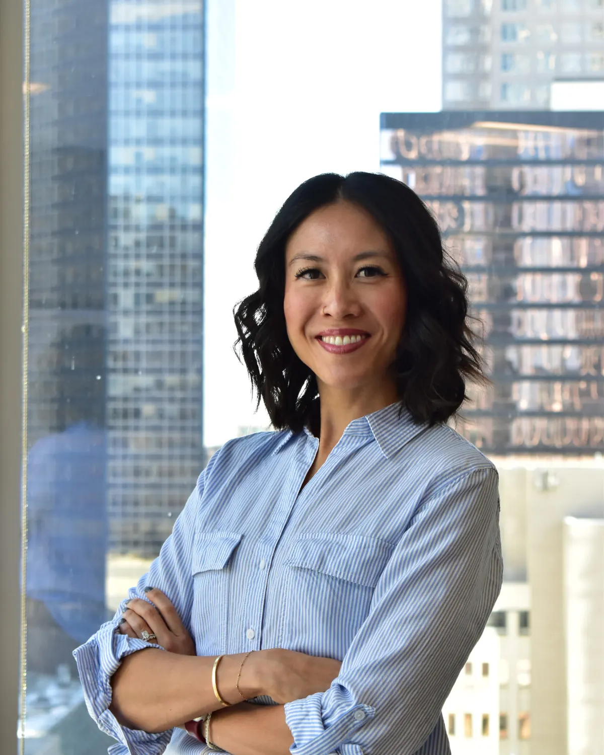 Denise Yee, founder of The Desine Co., standing with her arms folded in front of a downtown office window, smiling at the camera