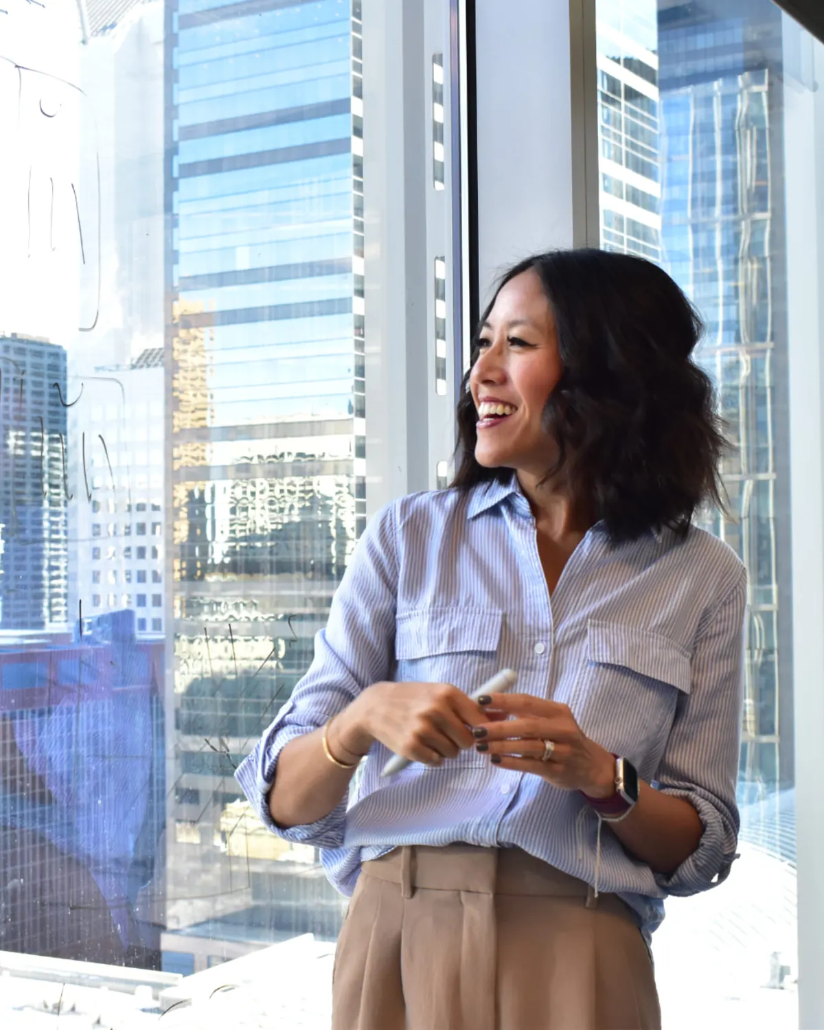 Denise laughing mid-conversation at a glass whiteboard covered in notes while a colleague takes notes beside her